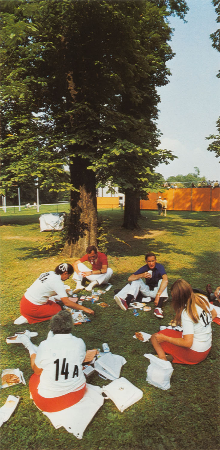 Fotografie einer Gruppe Menschen, die auf einer grünen Wiese sitzen und essen.