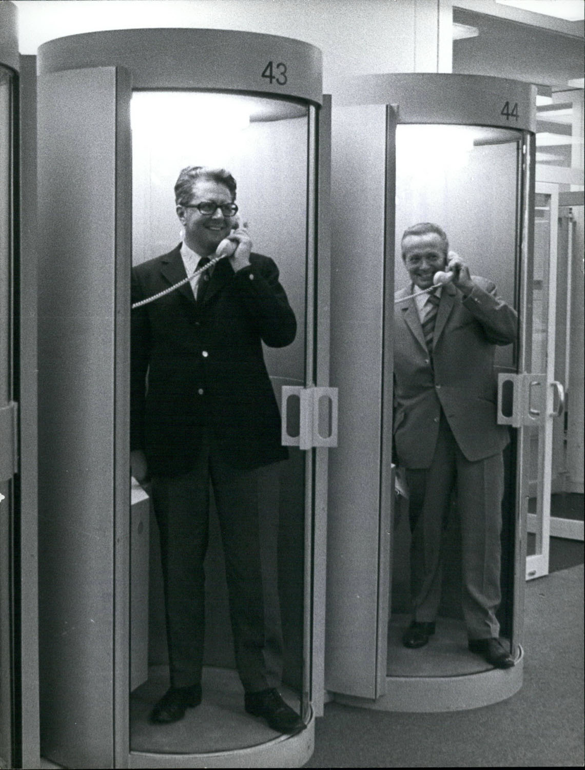 Schwarz-Weiß-Fotografie von zwei Männern die jeweils in einer Telefonzentrale telefonieren.