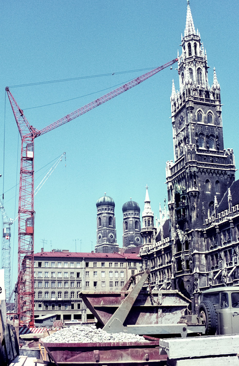 Fotografie einer großen Baustelle in der Innenstadt München. Im Hintergrund ein neugotischer Turm.