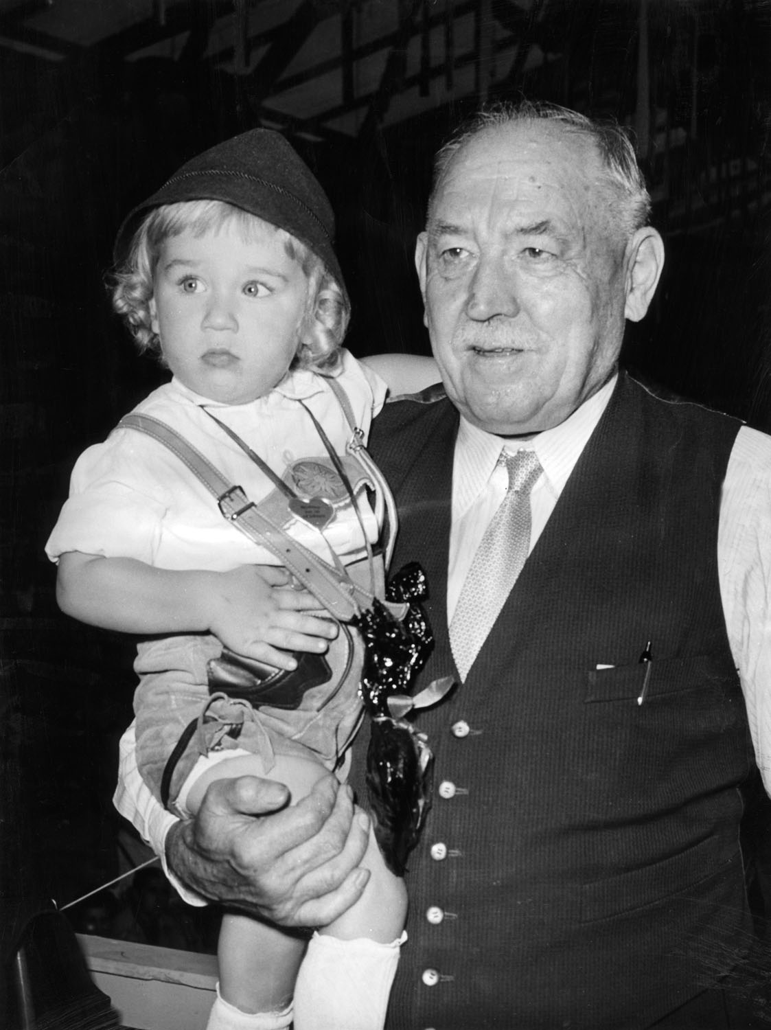 Schwarz-Weiß-Fotografie eines Mannes der ein Kleinkind auf dem Arm hält.