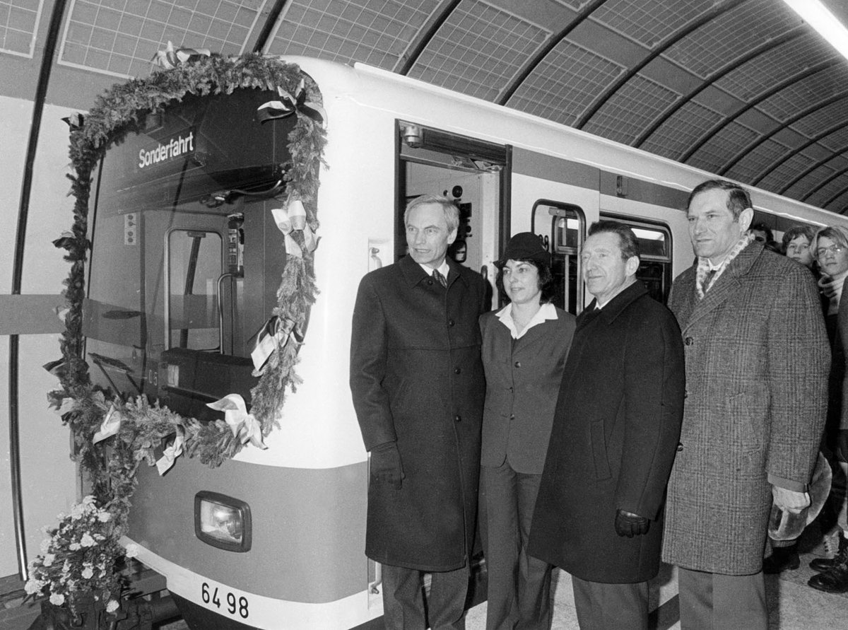 Schwarz-Weiß-Fotografie von vier Menschen, die neben einem U-Bahnzug stehen.