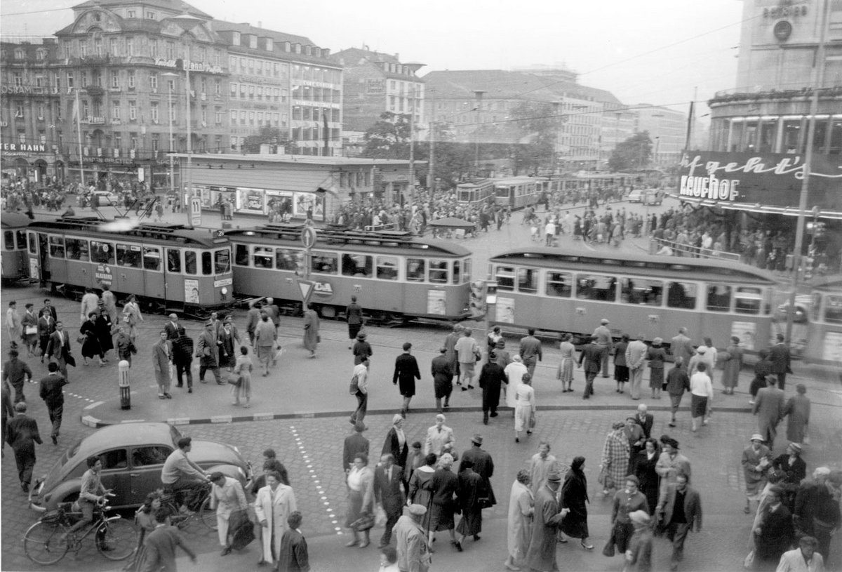Schwarz-Weiß-Fotografie der Innenstadt Münchens, mit Straßenbahnen und vielen Menschen.