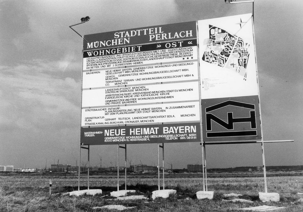 Schwarz-Weiß-Fotografie eines großen Bebauungsplans, aufgehängt an einem Gerüst auf einer Wiese.