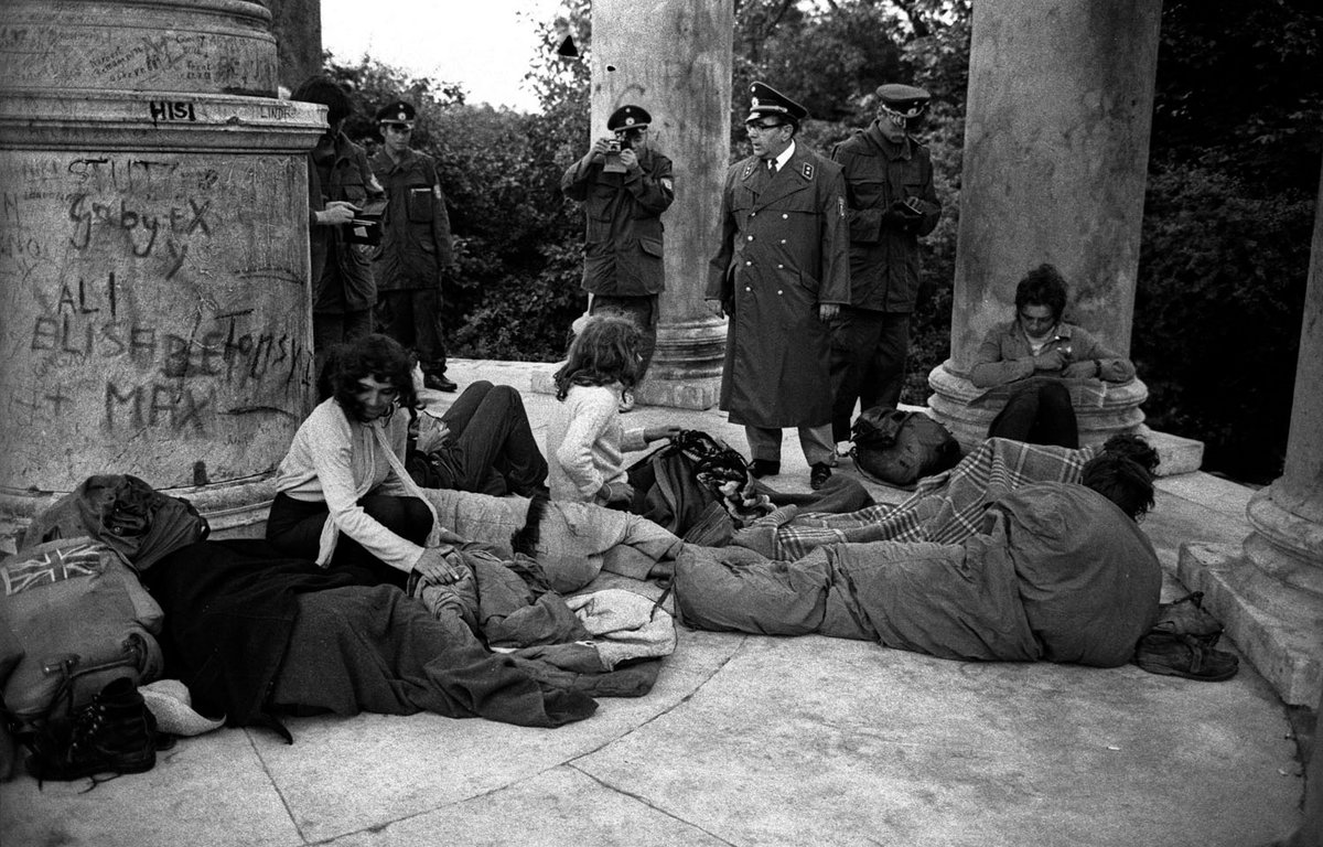 Schwarz-Weiß-Fotografie einer Gruppe von Frau die auf dem Boden sitzen. Im Hintergrund stehen Polizisten.