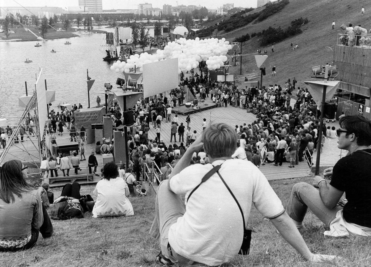 Schwarz-Weiß-Fotografie einer Menschenmenge die auf einem Berg sitzt.