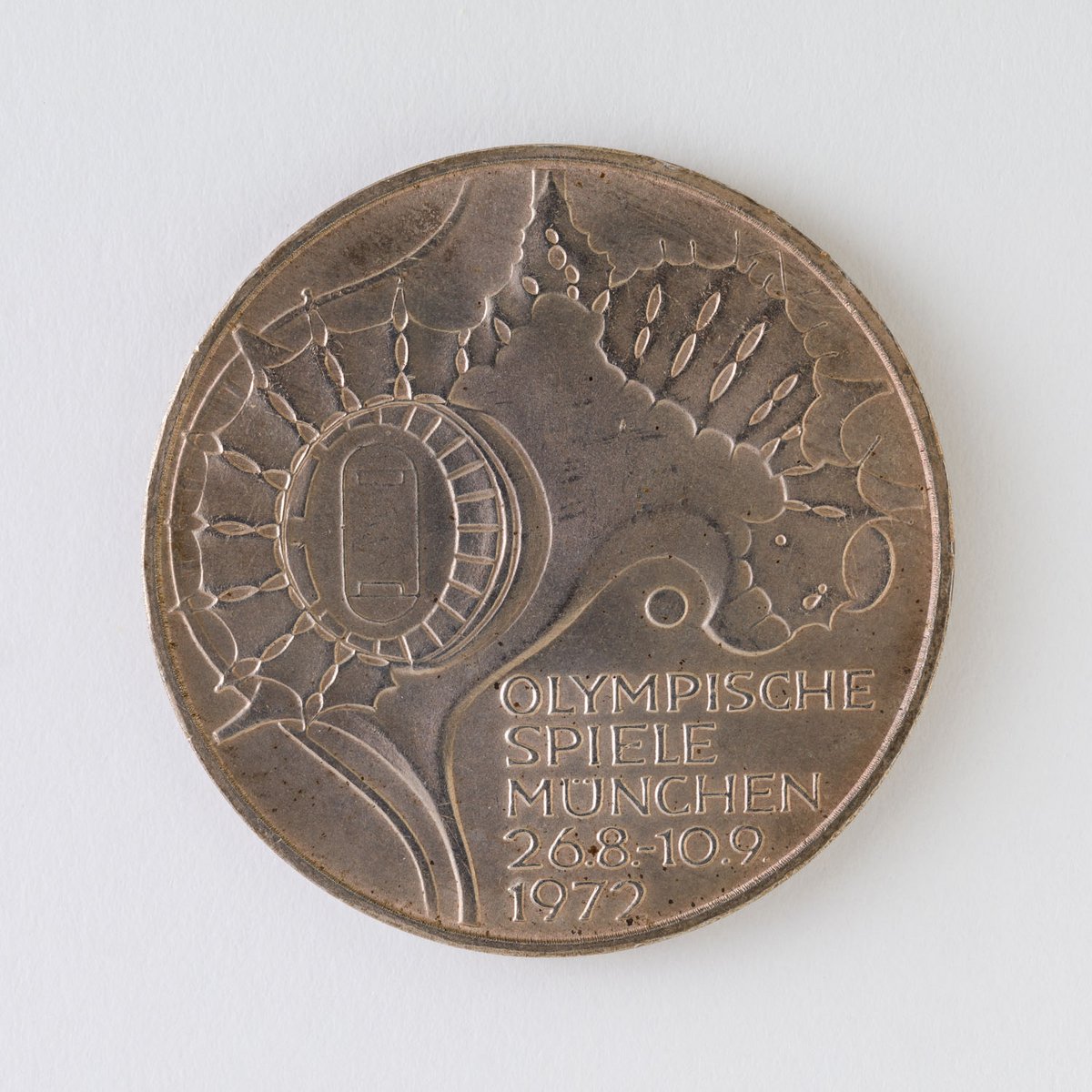 Eine bronzefarbige Münze mit dem Motiv eines Stadions