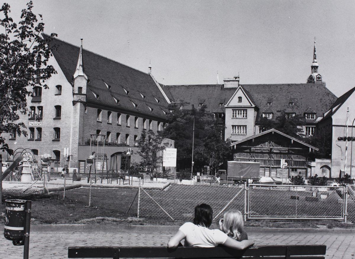 Schwarz-Weiß-Fotografie von einem Gebäude, im Vordergrund sitzen zwei Menschen auf einer Bank