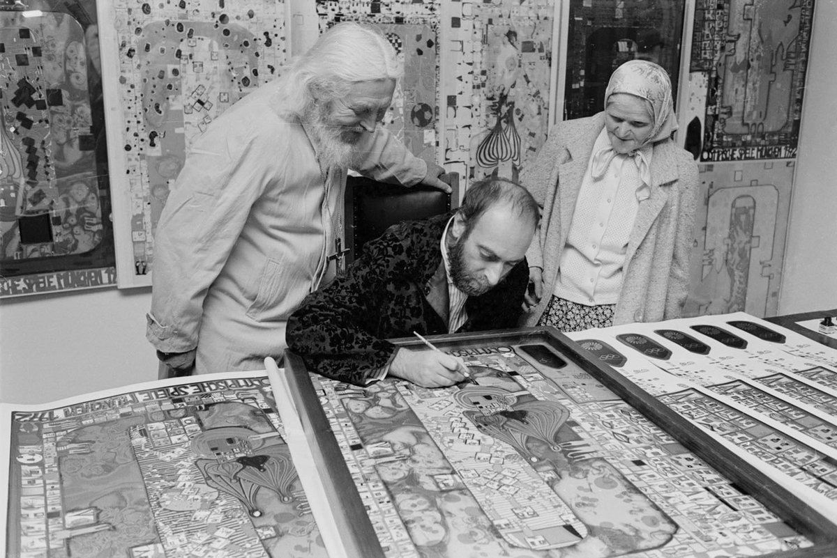 Schwarz-Weiß-Fotografie von drei Menschen. Ein Mann sitzt in der Mitte und zeichnet.