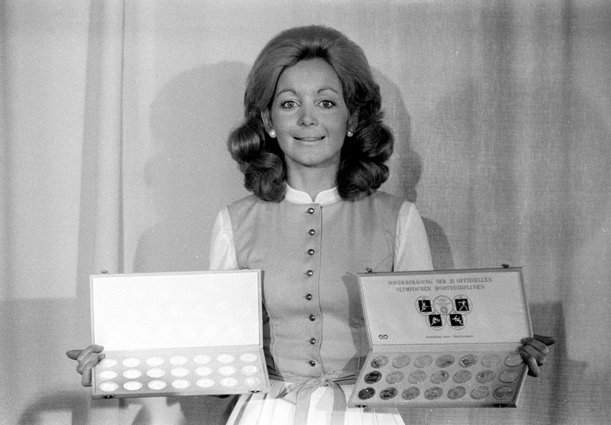 Schwarz-Weiß-Fotografie von einer Frau, die verschiedene Medaillen präsentiert.