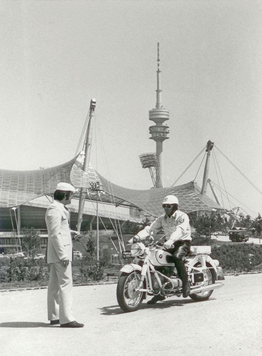 Schwarz-Weiß-Fotografie eines Mannes auf einem Motorrad der mit einem Fußgänger spricht