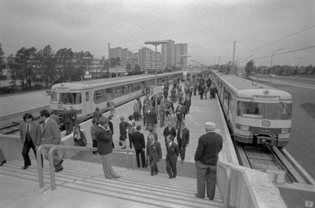 Schwarz-Weiß-Fotografie eines Bahnhofs mit vielen Passagieren und zwei Zügen.