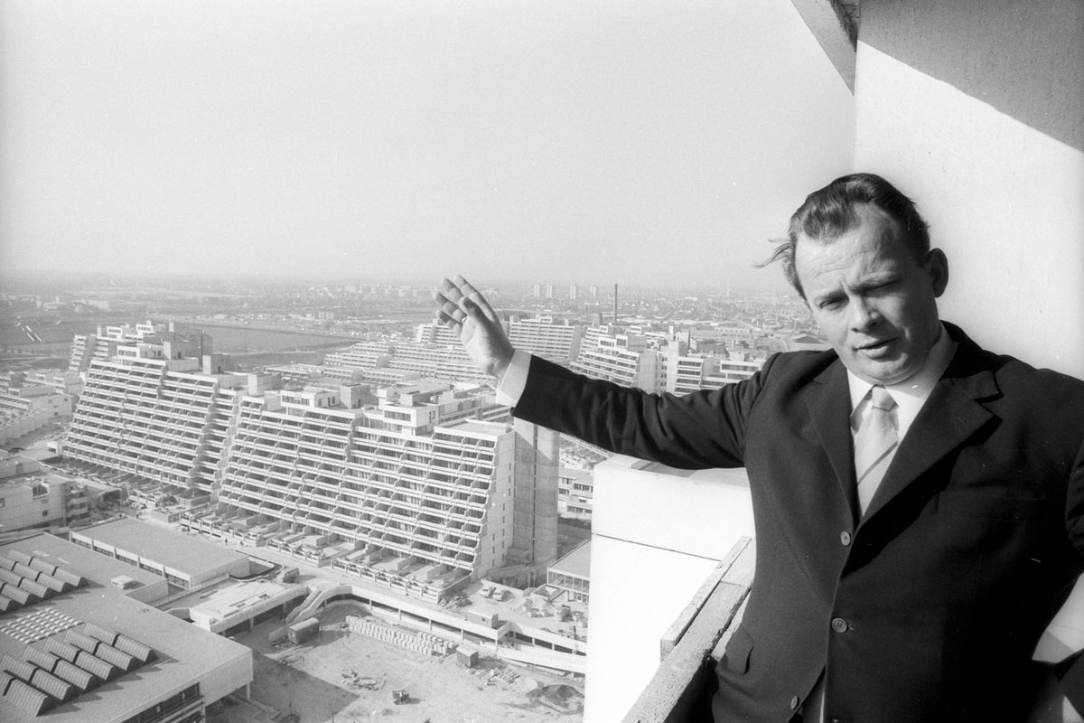 Schwarz-Weiß-Fotografie von einem Mann der zu einer großen Wohnsiedlung zeigt