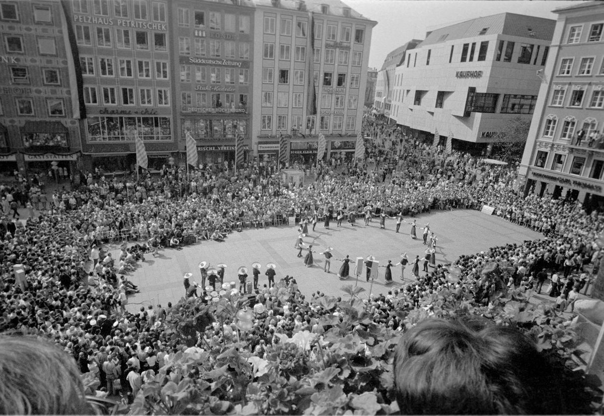 Schwarz-Weiß-Fotografie einer Gruppe Menschen, die vor Publikum im Reigen tanzt