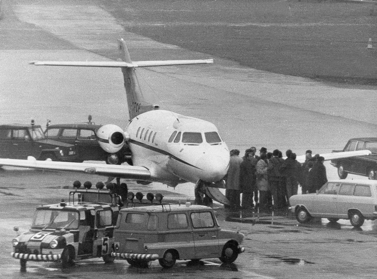 Schwarz-Weiß-Fotografie eines Flugzeuges und einer Gruppe Menschen.