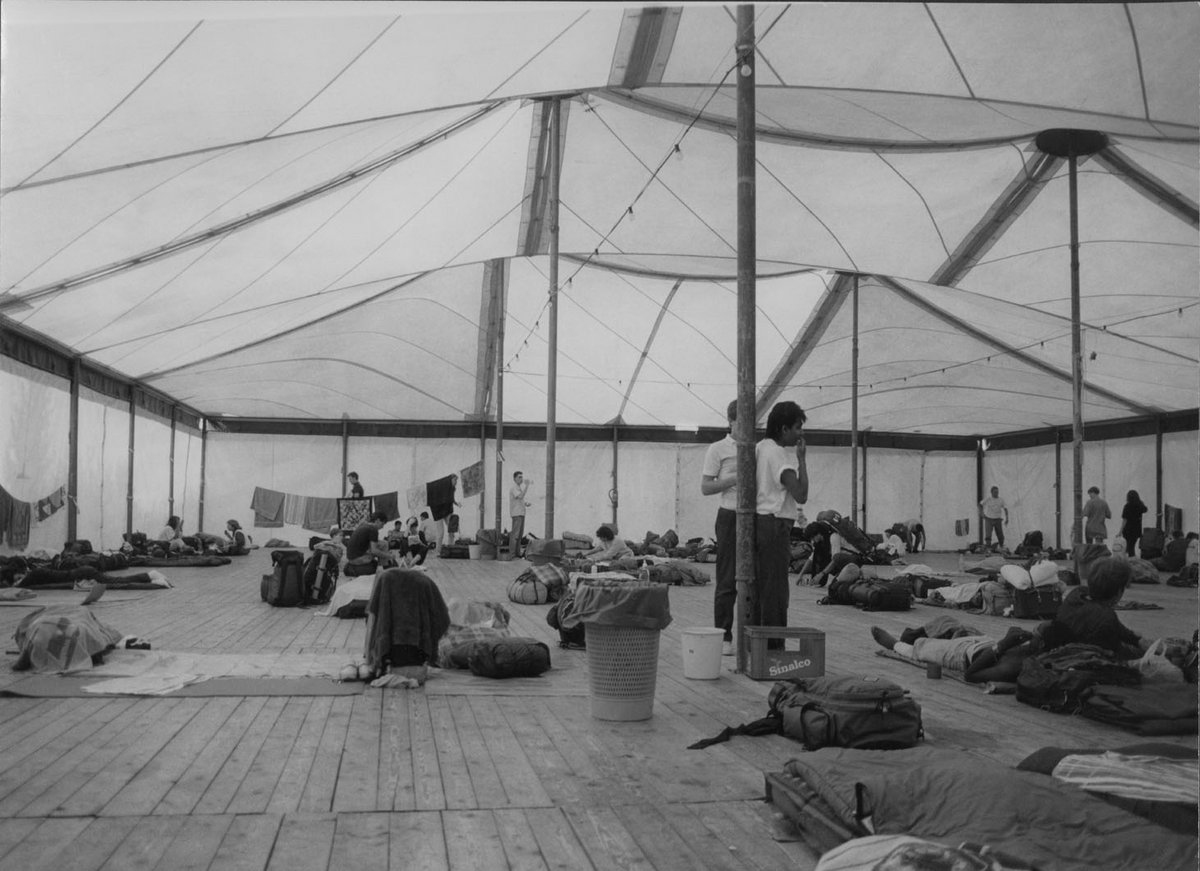 Schwarz-Weiß-Fotografie eines Zelts, darin liegen Schlafmatten und Rucksäcke.